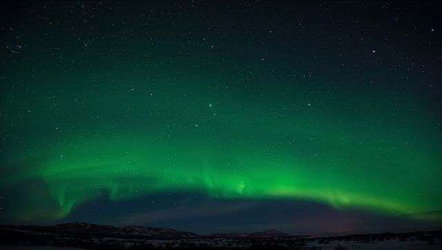 Dancing Green Aurora Stretching Over Snowy Arctic Tundra Under Starry Sky