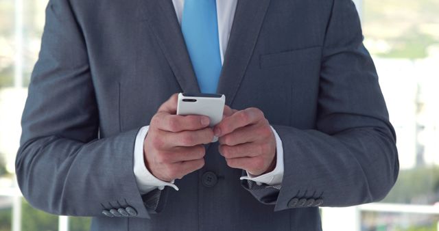 A Caucasian businessman in a suit is focused on texting on his smartphone, with copy space. His attire and engagement with the device suggest a professional setting, dealing with important communications.
