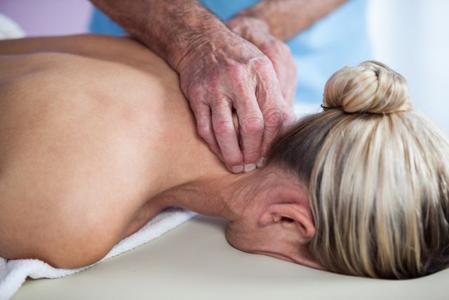 This image shows a woman receiving a neck massage from a physiotherapist in a clinic. It can be used for promoting wellness and healthcare services, illustrating physiotherapy techniques, or highlighting the benefits of professional massage therapy. Ideal for websites, brochures, and advertisements related to health and wellness, physical therapy, and stress relief.