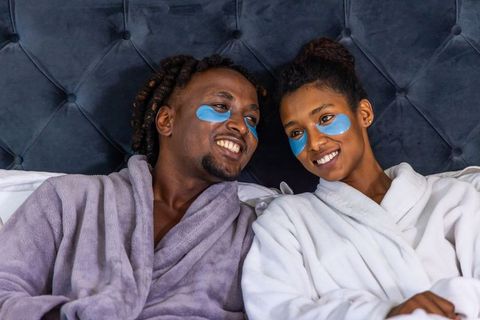 African american couple relaxing with blue under-eye gel patches wearing plush robes on bed