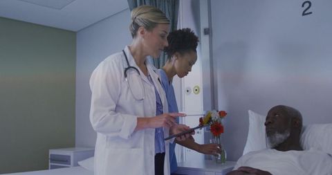 Doctor consulting tablet while nurse placing flowers at bedside with recovering patient