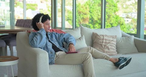 Relaxing man listening to music on headphones while reclining on contemporary light-gray sofa