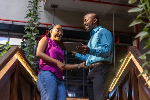 Smiling coworkers collaborate with tablet on urban staircase