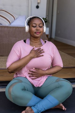 African american woman practicing mindful breathing with headphones, cross-legged at home