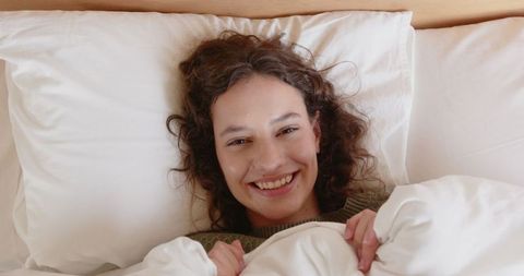 Smiling Woman Relaxing Under White Duvet at Home