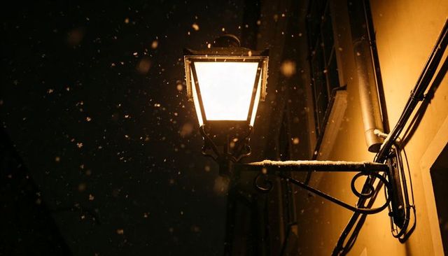Vintage Wall Lantern Illuminating Snowy Night Alley with Warm Glow and Iron Bracket