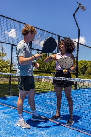 Playing padel on vibrant blue court with mixed-race friends exchanging rackets and smiles