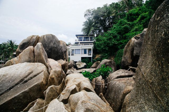 Secluded beach house nestled among large rocks and lush tropical greenery, ideal for portraying peaceful, exotic vacation scenes. Perfect for use in travel brochures, holiday destinations marketing, or promoting eco-friendly retreats.