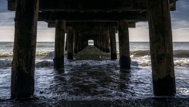 Framing Receding Wooden Pier Pillars Leading to Ocean Horizon with Rolling Waves and Foam