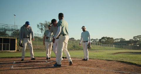 Diverse baseball teammates gathering at home plate on local diamond during practice