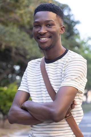 Smiling african american man standing with crossed arms wearing striped shirt and brown bag