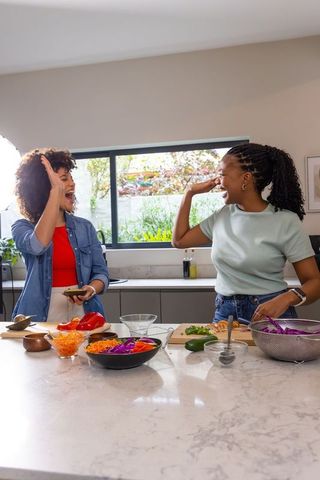 Diverse friends preparing colorful salad and high-fiving at sunlit marble kitchen island