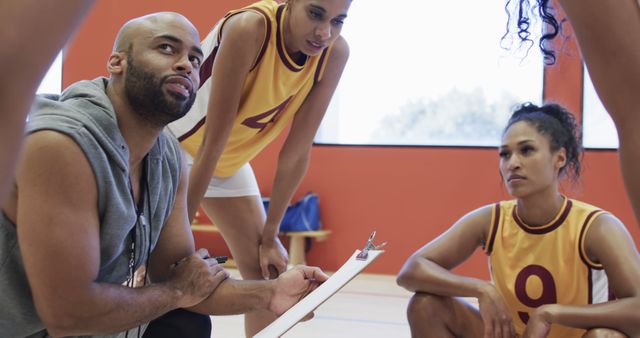 Basketball coach discussing strategy with female players on indoor court - Download Free Stock Images Pikwizard.com