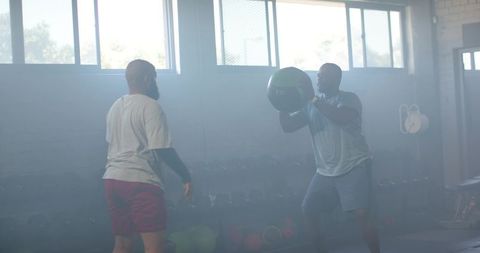 African american men doing partner medicine ball workout in industrial gym for strength