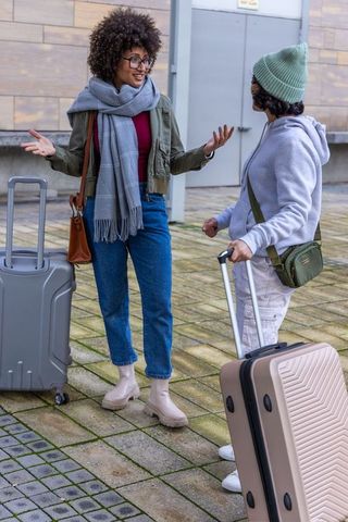Diverse friends chatting with rolling suitcases in urban plaza, casual travel reunion