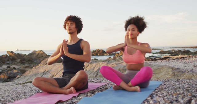 African american couple practicing yoga and meditating together on the rocks near the sea. love and relationship concept