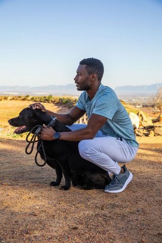 African american man pets black dog on trail under clear blue sky