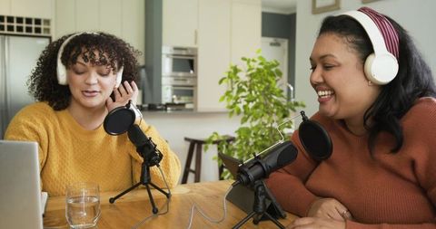 Cohosts recording conversational podcast in cozy kitchen with headphones and microphones
