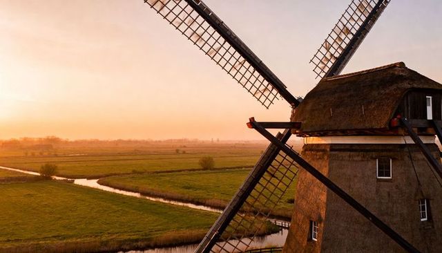 Turning thatched windmill over patchwork canals and green fields at golden hour