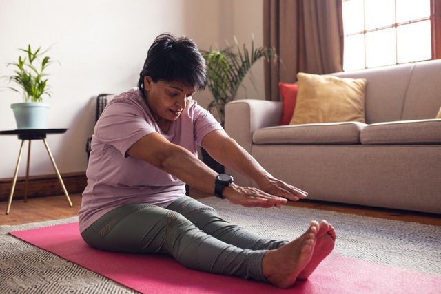 Mature woman with short hair stretching on a yoga mat in her living room. Ideal for promoting healthy and active lifestyles, home fitness routines, and wellness practices. Suitable for articles or advertisements related to yoga, retirement activities, and maintaining physical health at home.