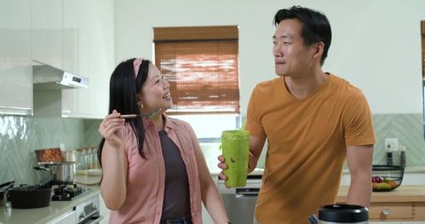 Asian couple enjoying homemade green smoothie in bright modern kitchen for wellness lifestyle