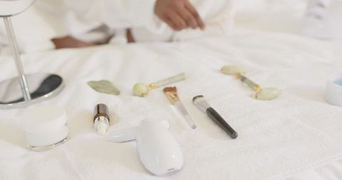 African woman in robe reaching for facial device and jade gua sha stones during home spa ritual