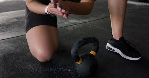 Kneeling athlete preparing with kettlebell and chalked hands