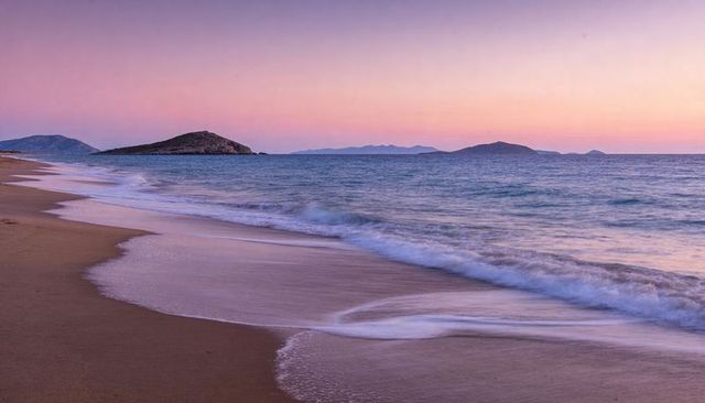 Sunrise waves washing pastel sandy beach with distant islets, tranquil seascape