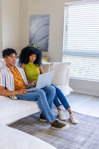 Asian man and african american woman using laptop on white sofa in modern living room