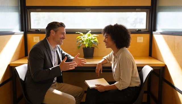Manager and colleague discussing project and taking notes in sunlit private office pod