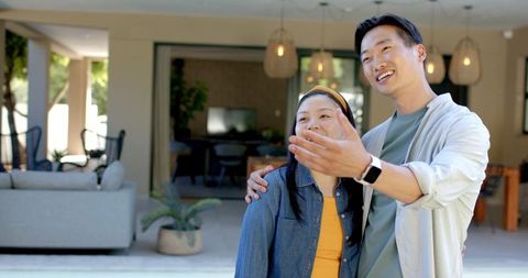 Asian couple touring modern open-plan home, pointing toward garden and patio