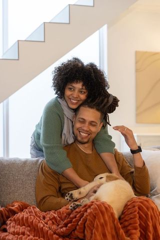 African american couple cuddling on sofa with sleeping puppy and cozy rust orange throw