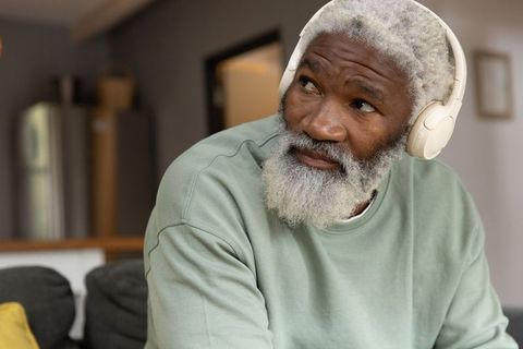 Senior african american man listening with headphones at home in open-plan living space