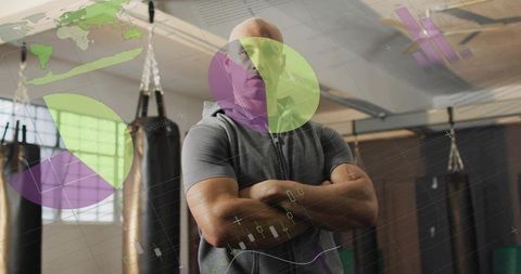 Confident trainer standing with arms crossed in boxing gym with fitness data overlay