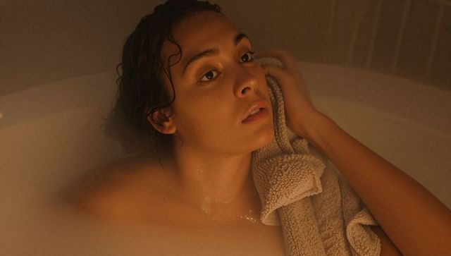 Young woman relaxing in milky bath holding towel, warm ambient glow, intimate self-care