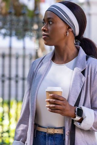 Urban professional african woman holding coffee, wearing smartwatch and striped headscarf