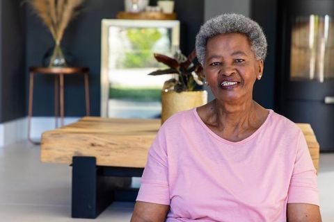 Senior african woman smiling while sitting in modern living room wearing pink top, warm portrait