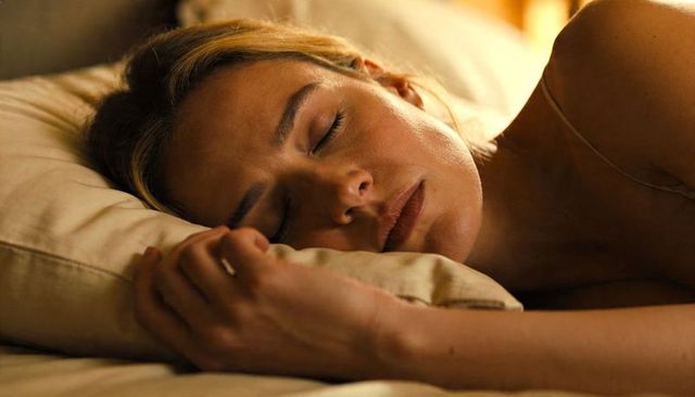 Sleeping woman resting head on pillow with ring, warm bedroom light, close-up lifestyle