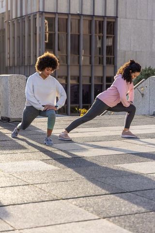 Two women stretching and lunging on urban terrace in morning sun for outdoor fitness