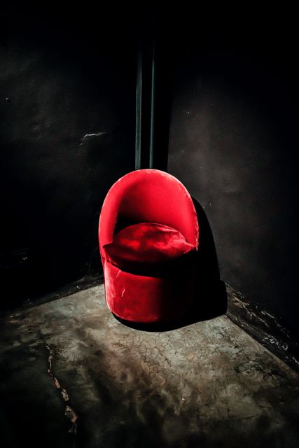 Red velvet armchair placed in dark minimalist interior, casting a dramatic shadow. Ideal for concepts related to luxury, modern living, elegance, and dramatic decor. Could be used in design magazines, interior decor blogs, or promotional material for furniture design.