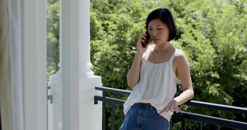 Woman Enjoys Sunny Day on Balcony While Talking on Smartphone