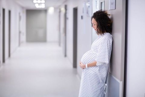 Pregnant Woman in Hospital Corridor Cradling Belly in Patient Gown