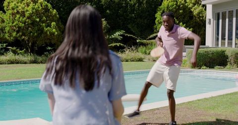 Diverse friends playing paddle ball by backyard pool