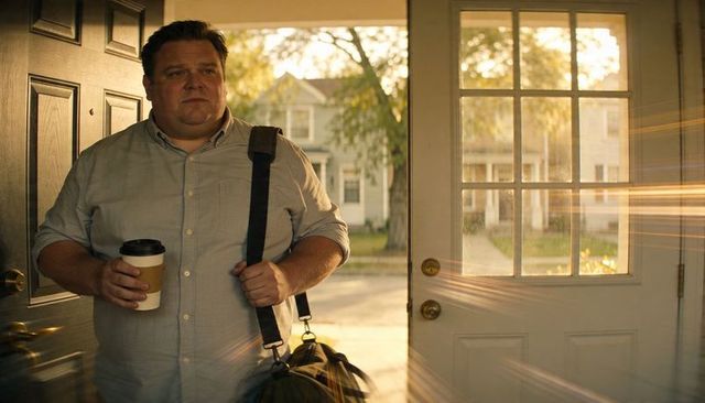 Man arriving home carrying coffee and duffel at sunlit front door, golden hour