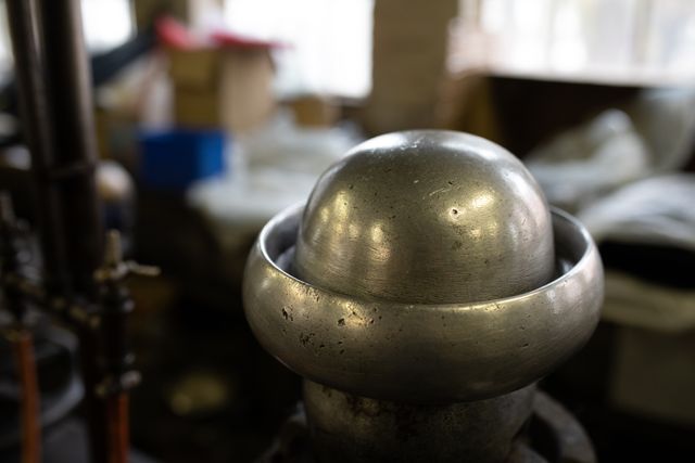 This image shows a close up of a shiny metal object used for creating hat shapes in a workshop at a hat factory. The background includes various tools and materials, indicating an active workspace. This image can be used for articles or advertisements related to hat manufacturing, craftsmanship, industrial processes, or artisan work.