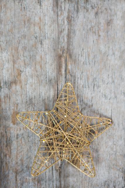 Golden star ornament placed on rustic wooden background, perfect for holiday-themed designs, Christmas cards, festive invitations, and seasonal marketing materials. The combination of the golden star and wooden texture adds a warm, rustic charm to any project.