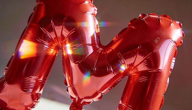 Glossy red foil letter m balloon reflecting prism light, close-up metallic monogram shimmer