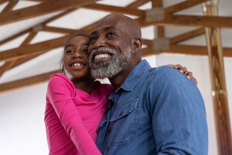 African american father hugging daughter and smiling under wooden beams in bright hall