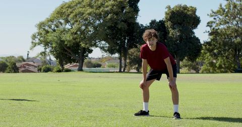 Curly-haired teen catching breath after sprinting on sunlit park field during training