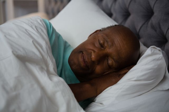 Senior man sleeping peacefully on bed at home, showcasing relaxation and comfort. Ideal for use in articles about sleep health, elderly care, home living, and lifestyle. Can be used in advertisements for bedding, sleep aids, and wellness products.